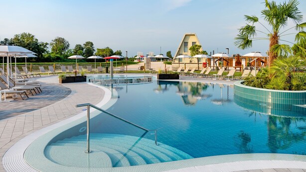 A swimming pool with sun loungers and umbrellas, surrounded by a landscaped area with palm trees.