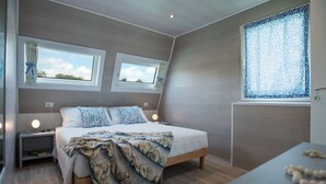A bedroom with a bed, two bedside tables, a nightstand, a window with curtains, and a decorative wall panel.