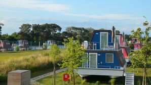 A row of blue and red floating homes with a grassy path leading to them, surrounded by trees.