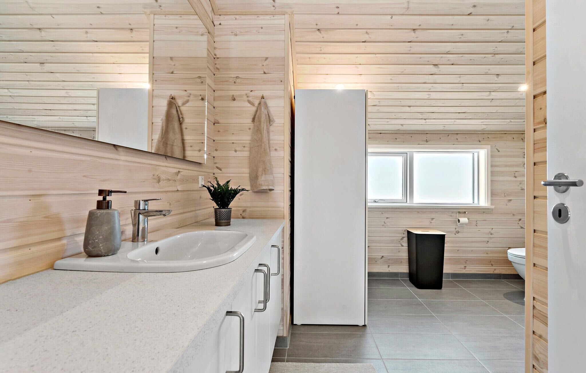 Un baño moderno con paneles de madera, un lavabo con dispensador de jabón, una planta en maceta y un inodoro.