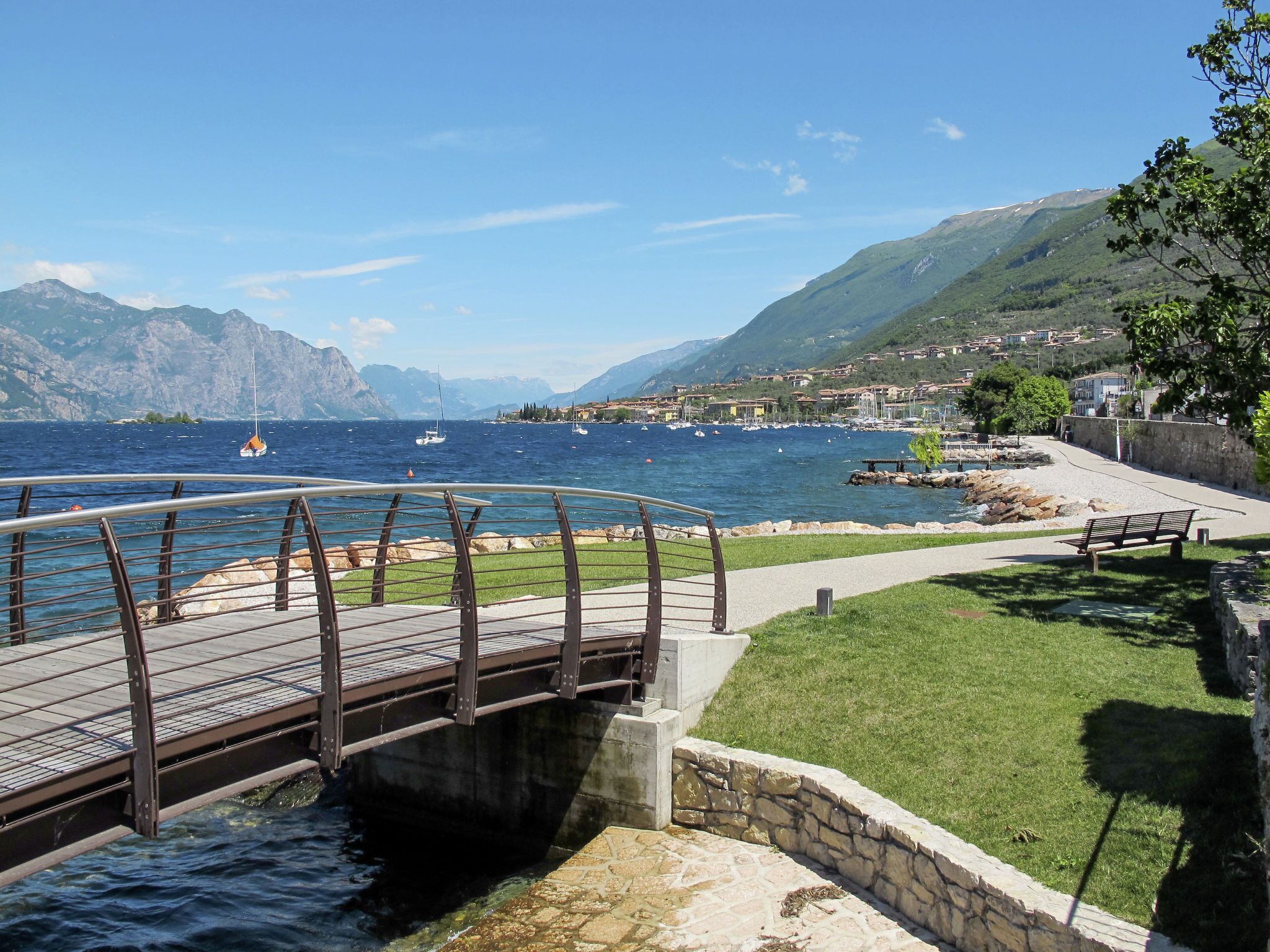 Un ponte di legno sopra l'acqua, una zona erbosa e un muro di pietra con una panchina.