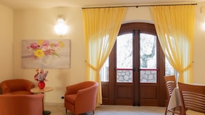 A room with a wooden door, yellow curtains, a painting of flowers, and orange chairs. - Casa Maria by Interhome (Brenzone)