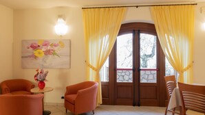 Una habitación con puerta de madera, cortinas amarillas, un cuadro de flores y sillas naranjas.