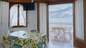 Ein Essbereich mit Tisch, bedeckt mit einem Zitronenmuster, einem an der Wand befestigten Fernseher und einem Balkon mit Blick auf Berge und einen See.