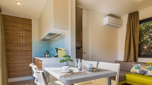 Une cuisine moderne avec des meubles blancs, une table à manger avec des chaises, une petite plante et une fenêtre avec des rideaux.