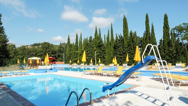 Una piscina con tobogán, tumbonas y sombrillas amarillas.