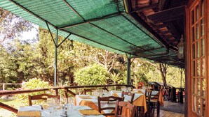 Un área de comedor al aire libre con mesas dispuestas para los comensales, rodeada de exuberante vegetación y una estructura de techo cubierta.