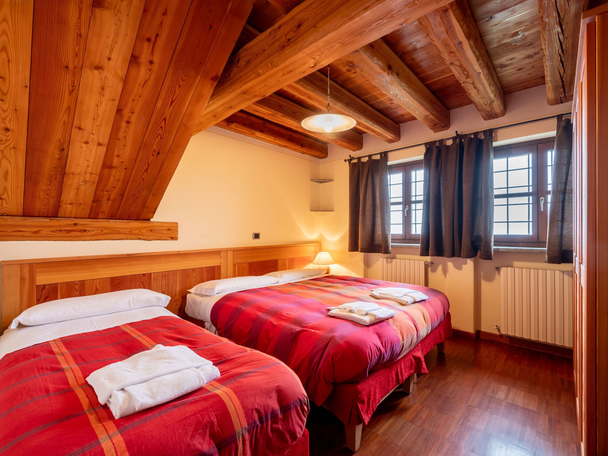 Ein Zimmer mit zwei Betten, Holzbalken, einem fenster mit Vorhängen und einer Heizung.