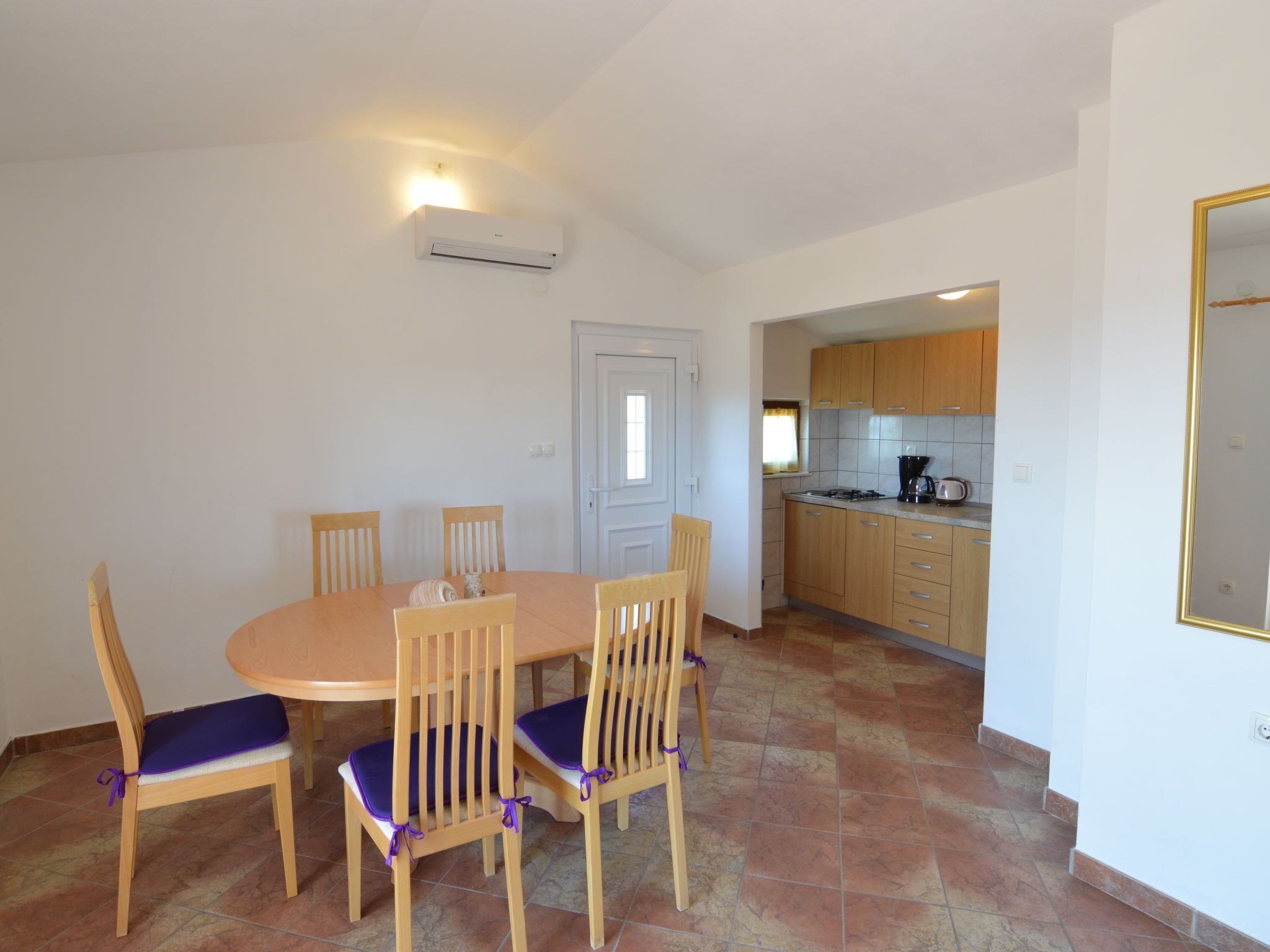 Un coin repas avec une table ronde et six chaises, une cuisine dotée de meubles en bois et un climatiseur fixé au mur.