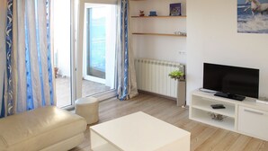 A modern living room with a sofa, a white coffee table, a TV on a stand, and a view of the outdoors through a glass door. - Andriana by Interhome (Šibenik)