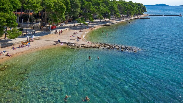 Ein Strand mit klarem Wasser, Bäumen und Menschen.