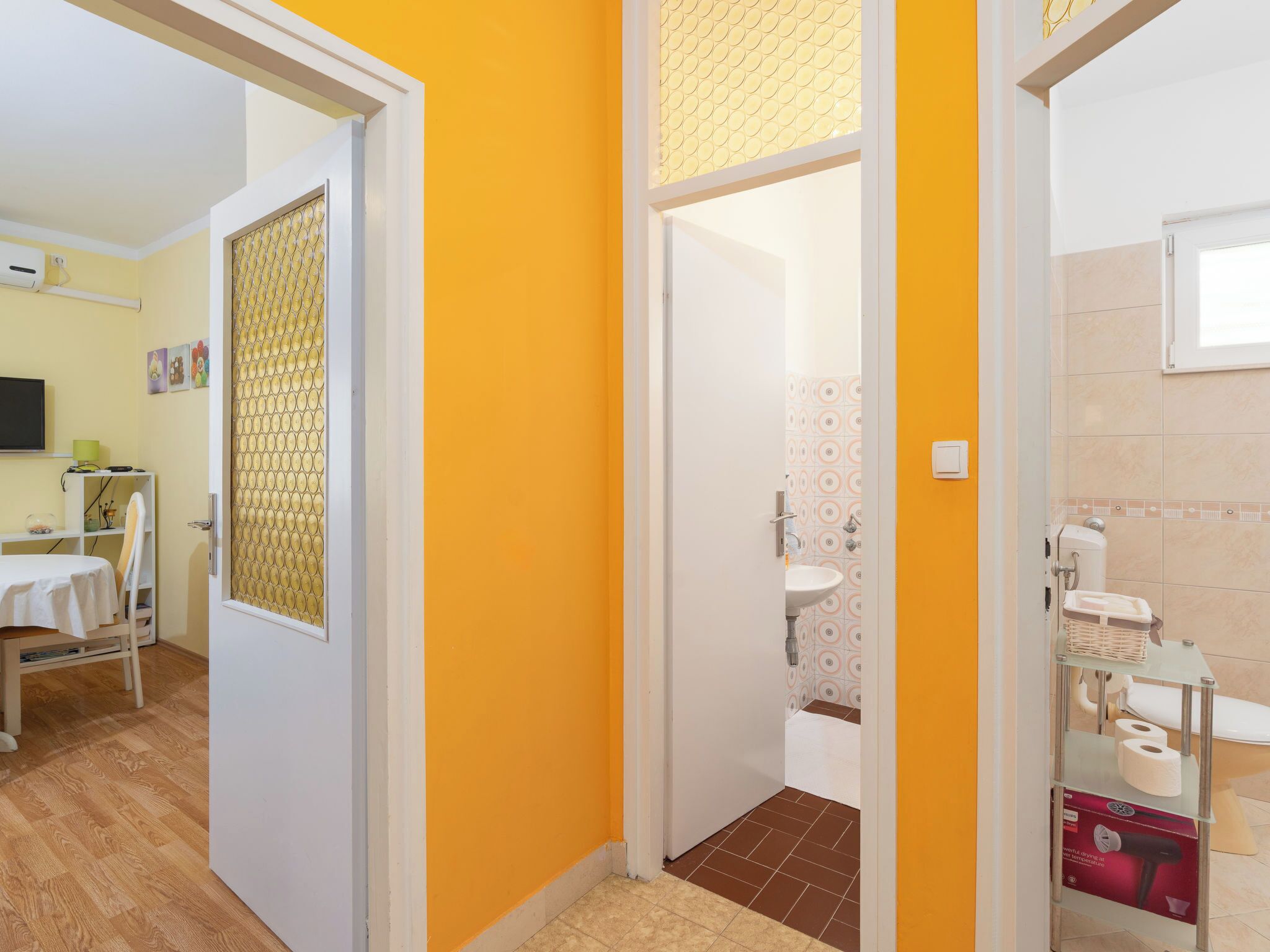 A hallway with a yellow wall, a door leading to a bathroom, and a shelf with toiletries.