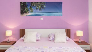 Ein Schlafzimmer mit einem Bett, zwei Nachttischen, einem an der Wand befestigten Bild von einem Strand und einer gemusterten Bettdecke.