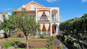 Ein zweistöckiges Gebäude mit Balkon, umgeben von Grünflächen und einem Garten.