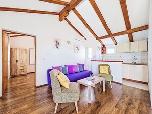 Een kamer met een houten plafond, een paarse bank, een kleine tafel en een keukenhoek.