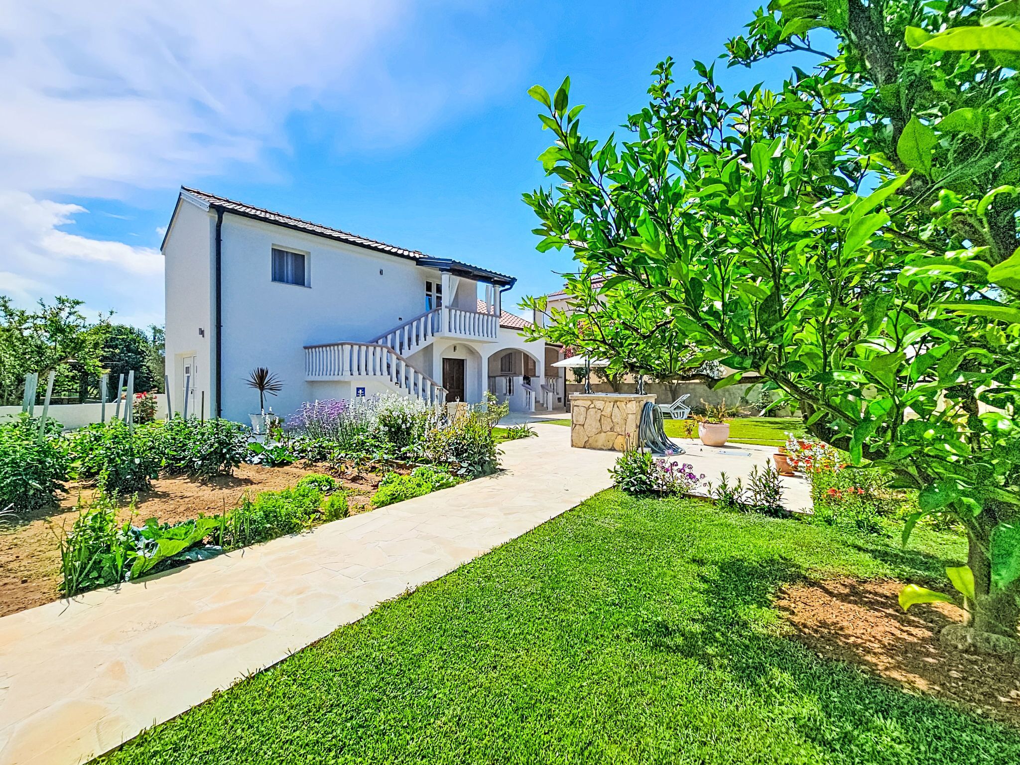 A white two-story house with a stone pathway leading to the entrance, surrounded by well-maintained gardens and a clear blue sky.