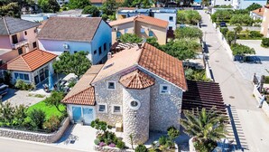 A coastal town with stone buildings, a clear blue sea, and a paved street.