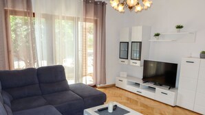 Een moderne woonkamer met een grijze bank, een televisie op een witte dressoir en een houten vloer.
