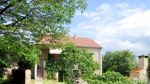 Una casa di pietra con tetto in tegole, immersa nel verde e circondata da un muro in pietra.