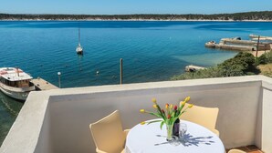 Eine Terrasse mit Tisch für Zwei, mit Blick auf ein ruhiges Meer und ein in der Nähe liegendes Boot.