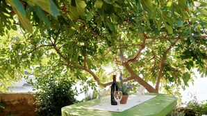 A green outdoor bar with a bottle of wine and glasses on a table, surrounded by lush foliage and a view of boats on the water. - Apartment Ana by Interhome (Rab/Rab)