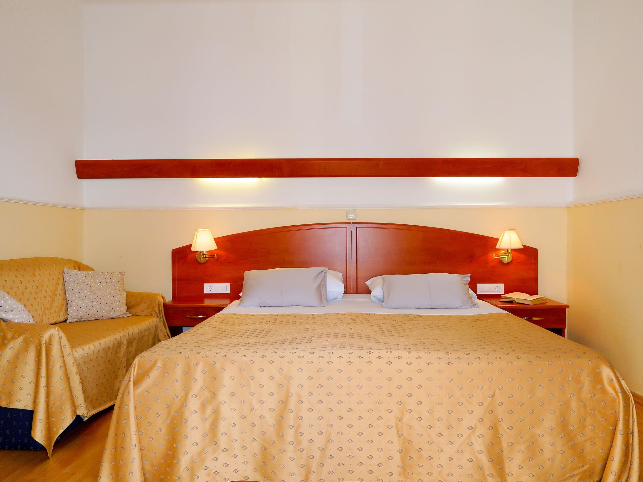 Een hotelkamer met een groot bed, twee nachtkastjes met lampen, een houten hoofdbord en een stoel met een gestreept kussen.