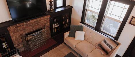 A living room with a flat-screen TV, a fireplace, a sofa, and a window with a view.