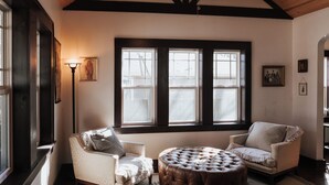 A room with two armchairs, a round ottoman, and a large window with dark frames. - Tranquil Pet-Friendly Bungalow in Midtown Springfield with High-Speed Wi-Fi (Springfield)