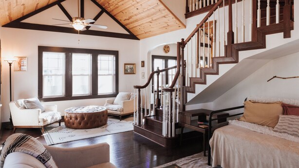 A spacious living room with a high ceiling, a wooden staircase, and a cozy seating area with a round ottoman. - Tranquil Pet-Friendly Bungalow in Midtown Springfield with High-Speed Wi-Fi (Springfield)