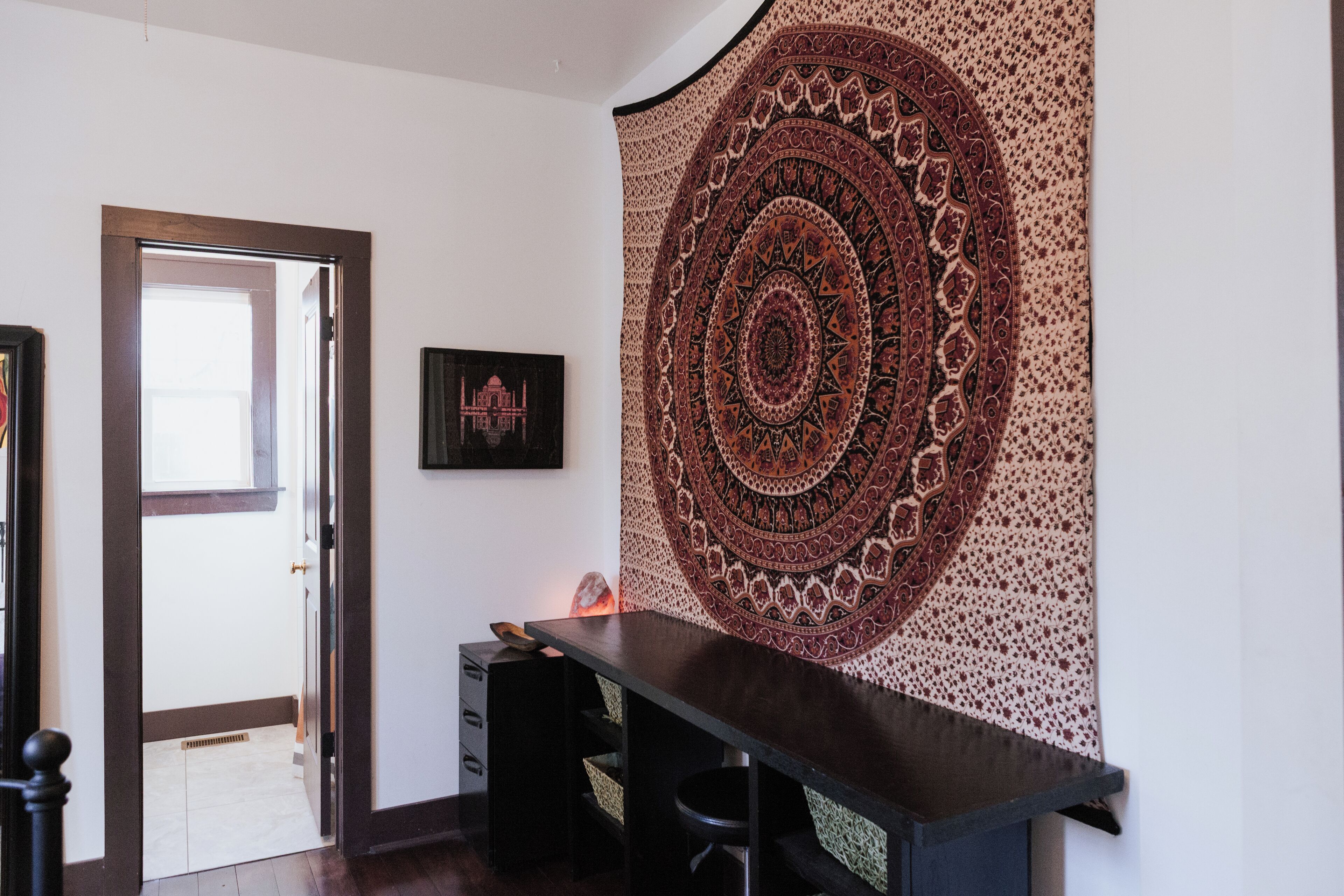 Une pièce avec un bureau en bois foncé, une tapisserie ornée d’un motif circulaire et un tableau encadré accroché au mur.