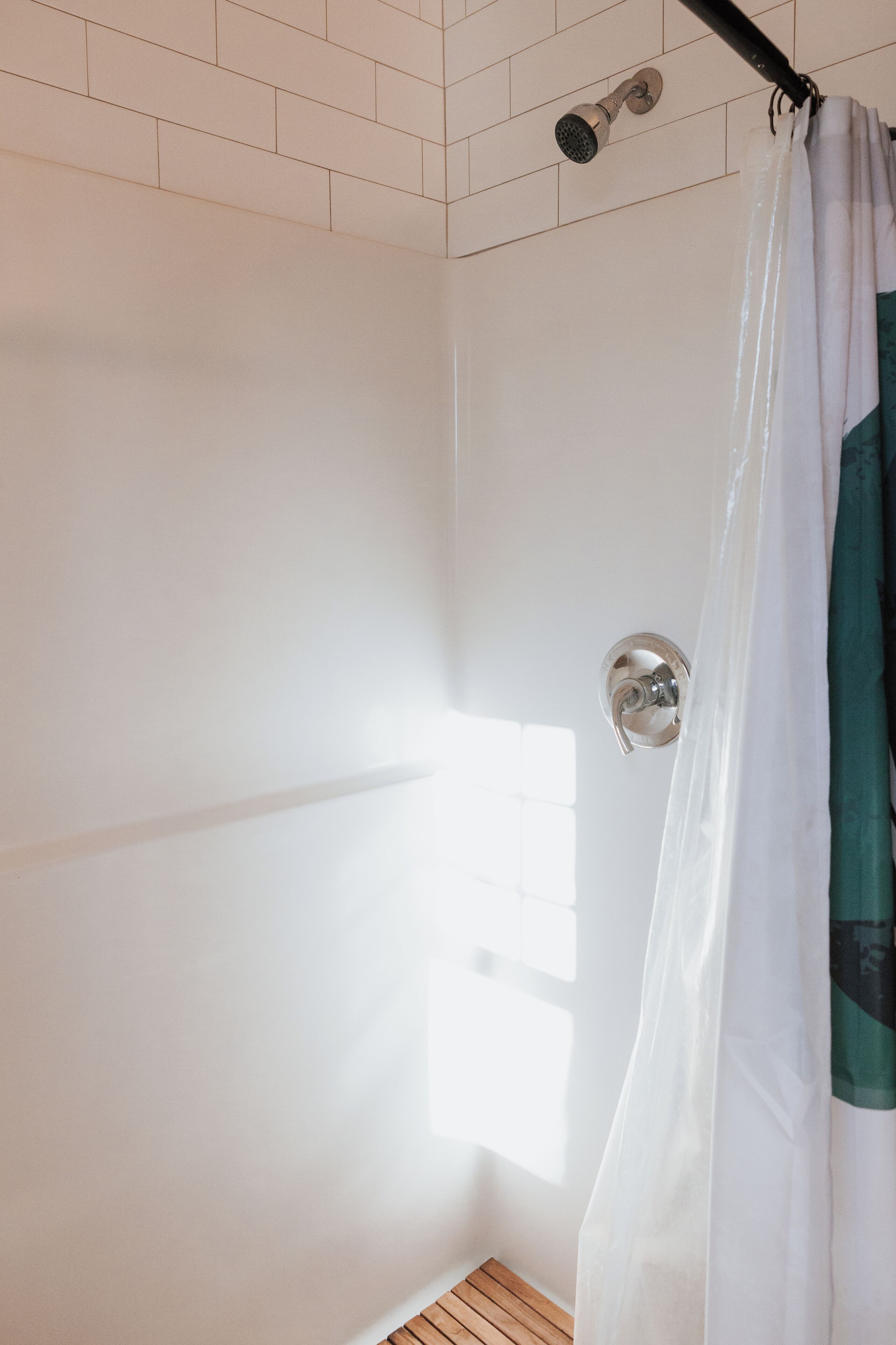 A shower with a white curtain and a handheld showerhead.