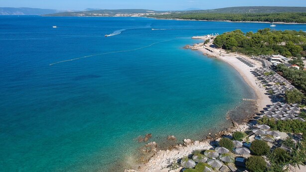 An aerial view of a coastal area with a clear blue sea, a sandy beach with umbrellas, and a small town in the background. - Apartment Vesna by Interhome (Krk/Punat)
