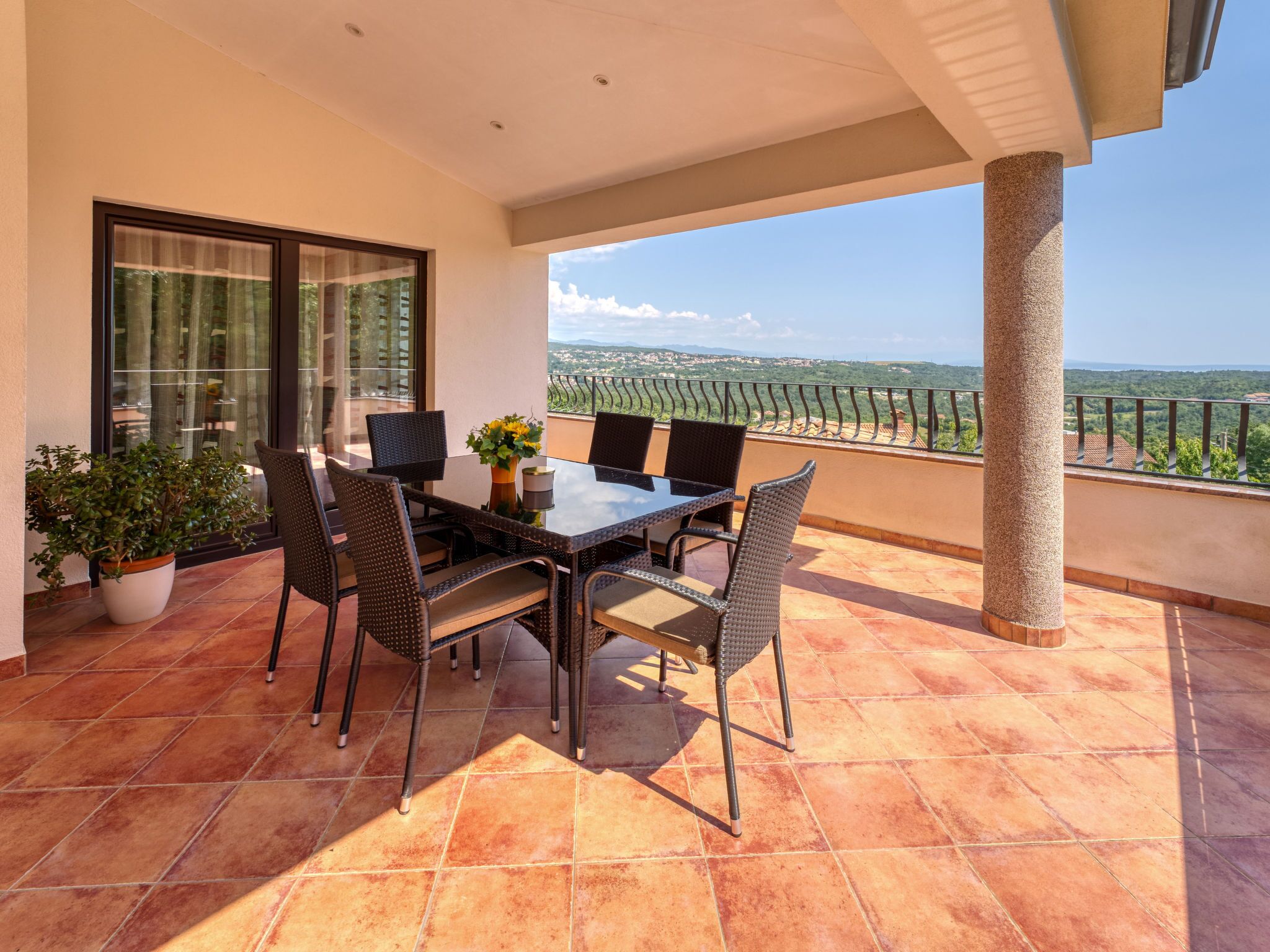 A balcony with a dining table and chairs, a potted plant, and a view of the landscape.