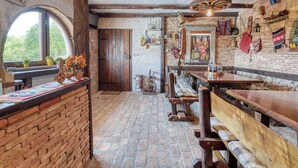 Un intérieur rustique avec des murs en briques apparentes, des poutres en bois, un coin bar avec des tabourets et une grande fenêtre.
