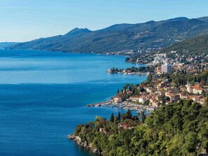Uma cidade costeira com um porto de iates, edifícios e montanhas ao fundo.