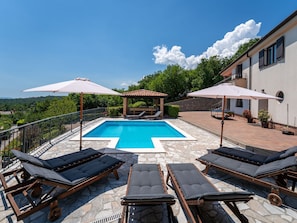 Un espace piscine aménagé avec des chaises longues, des parasols et offrant une vue sur le paysage environnant.