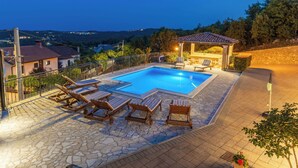 Une piscine avec des chaises longues, un espace salon couvert et une terrasse en pierre.