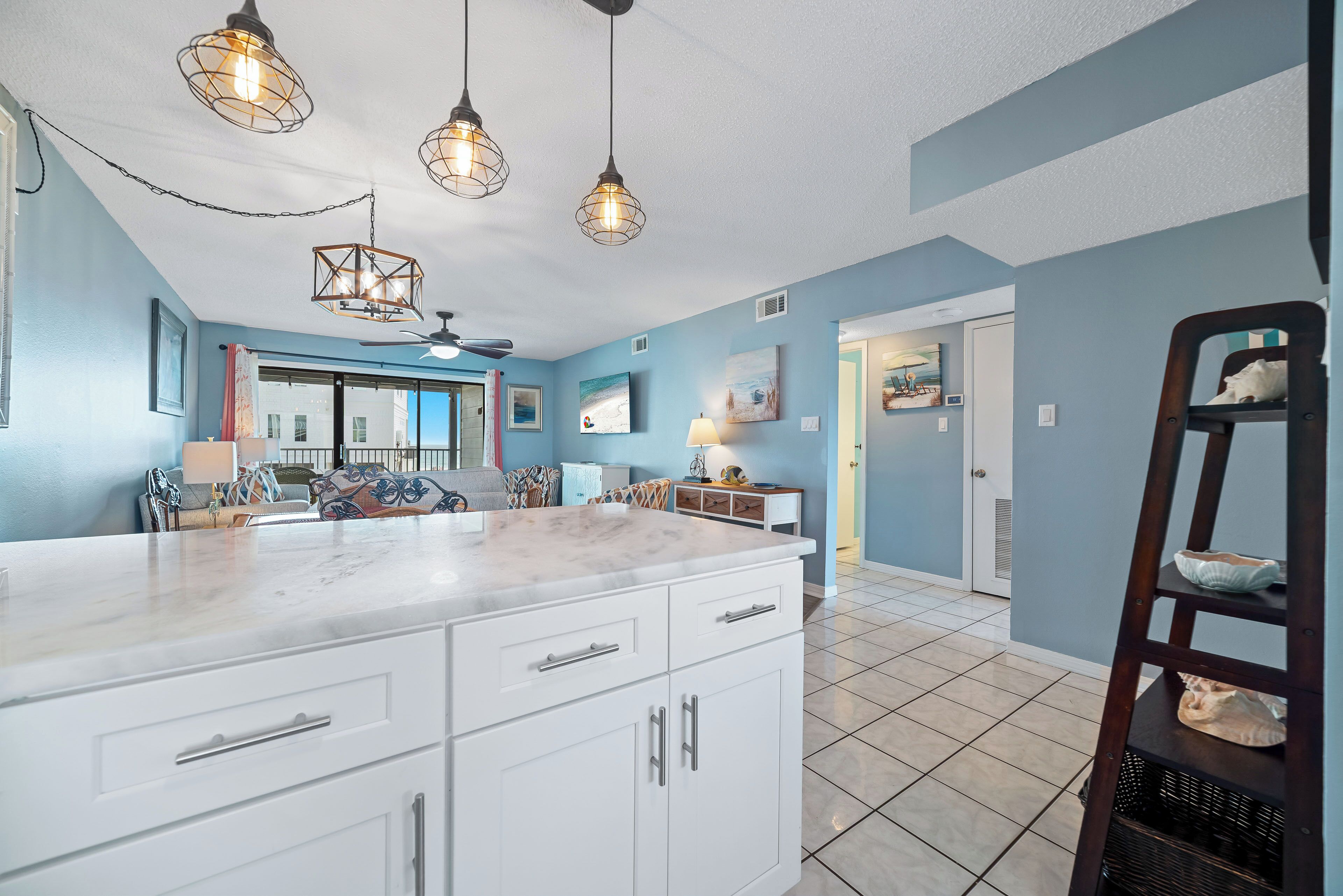 A kitchen with white cabinets, a marble countertop, and pendant lighting.