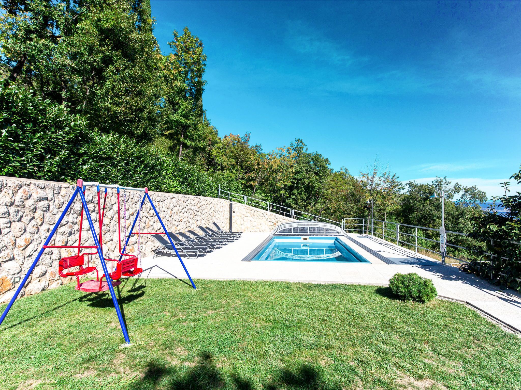 A swimming pool with a stone wall and a grassy area.