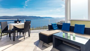 A terrace with a table and chairs, a sofa, and a glass-top coffee table, overlooking a body of water and distant hills. - Filip & Katja by Interhome (Mošćenička Draga)