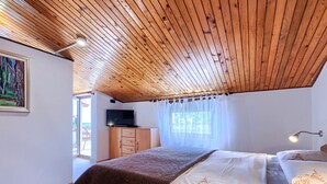 A bedroom with a wooden ceiling, a bed with white and brown bedding, a TV on a wooden cabinet, and a window with sheer curtains. - Vacation home Lancin by Interhome (Pula/Marčana)