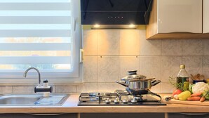 Une cuisine moderne équipée d’une cuisinière à gaz, d’un évier et d’une fenêtre avec des stores.