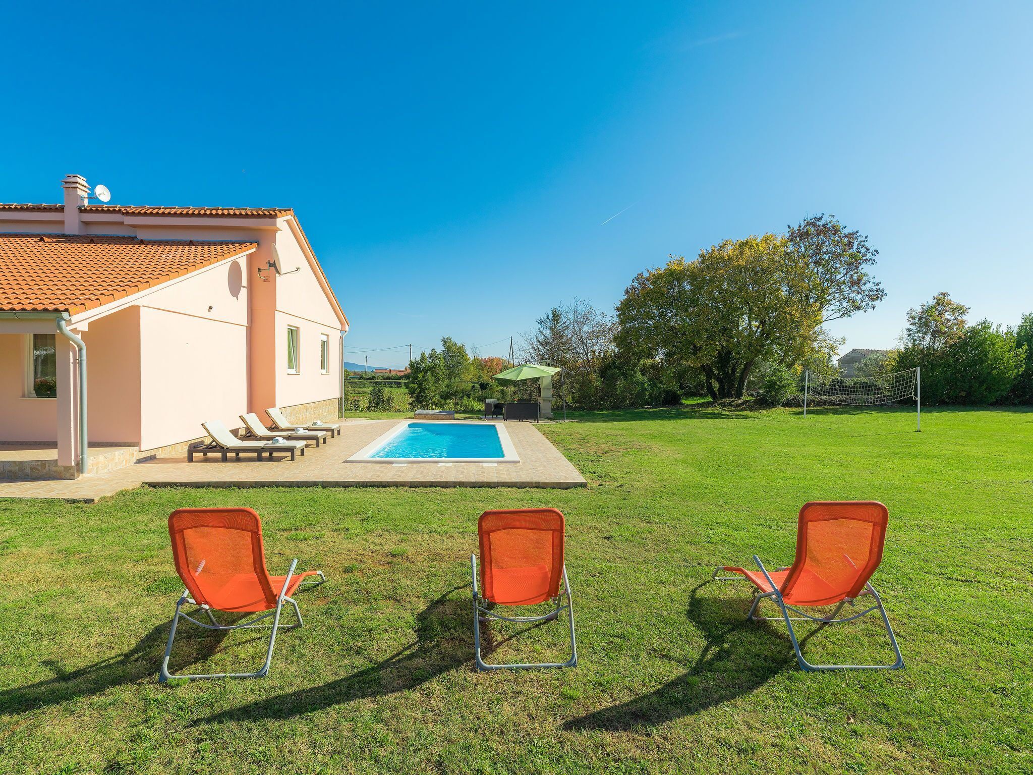 A house with a swimming pool, two orange chairs, and a tennis court.