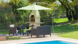 Un espace aménagé au bord de la piscine, avec un barbecue, des sièges d’extérieur et une piscine à l’eau d’un bleu limpide.