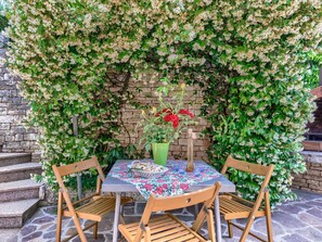 A round table with a floral tablecloth, two wooden chairs, and a vase with flowers.