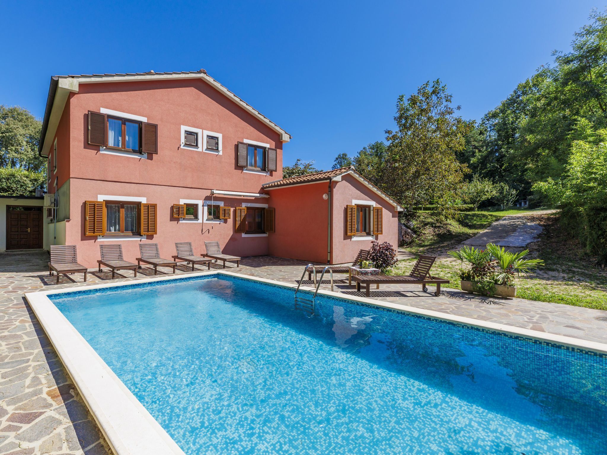 Una casa de dos pisos con piscina, mobiliario exterior y jardín.