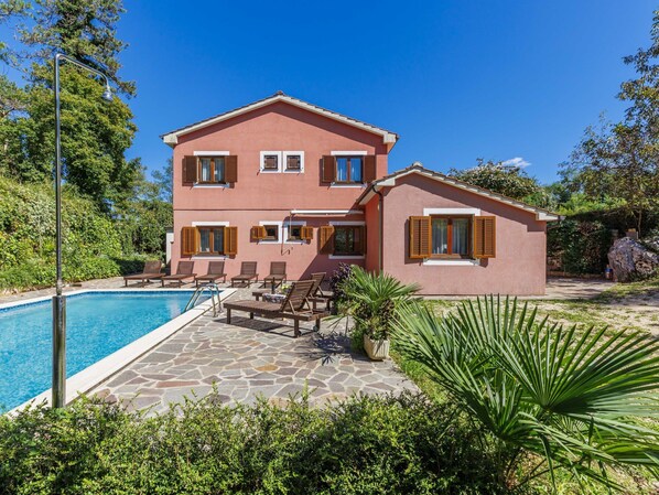 A two-story house with a swimming pool, outdoor seating, and a garden.