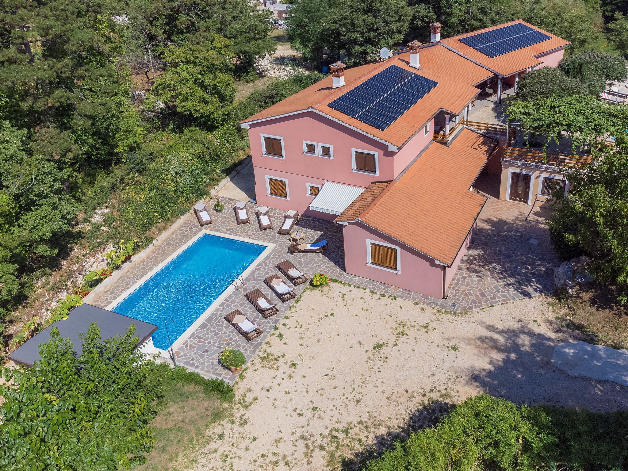 Una casa de dos pisos con piscina, paneles solares y jardín.