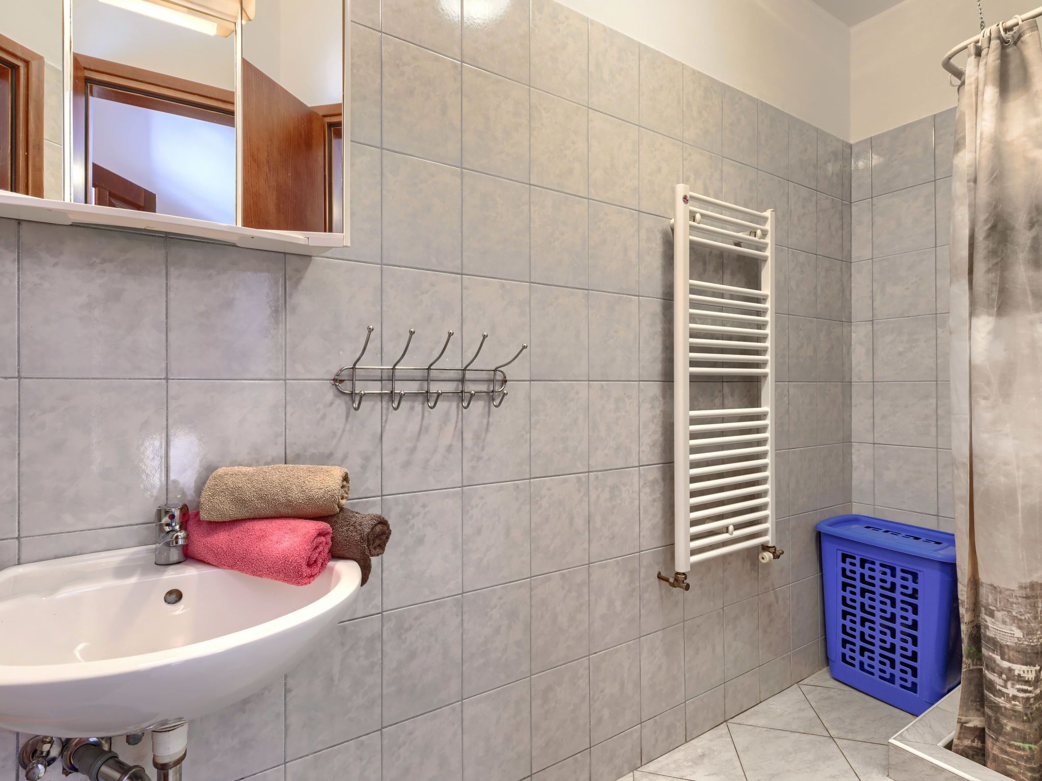 Une salle de bain équipée d’un lavabo, d’un porte-serviettes, d’une douche et d’un panier à linge bleu.
