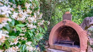 A brick-built outdoor oven with a stone base, surrounded by lush greenery.